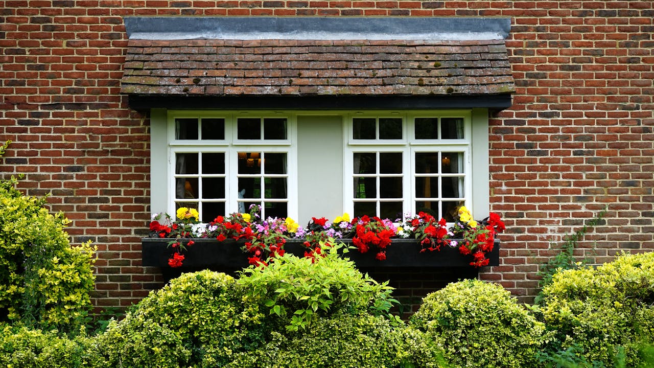 Brick cottage window adorned with colourful flowers and lush greenery