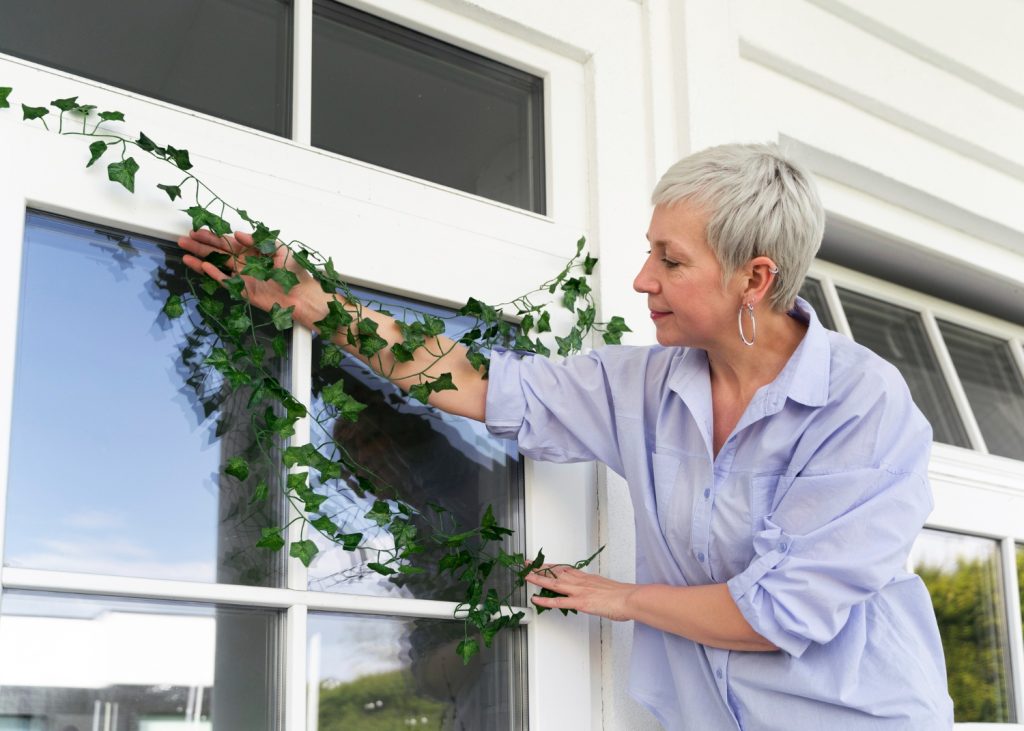 Woman in a light blue shirt arranging ivy on a white window frame