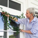 Woman in a light blue shirt arranging ivy on a white window frame