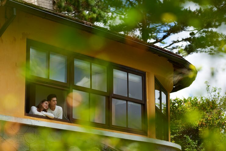 Couple enjoying a scenic view from a window in a round yellow house, surrounded by lush greenery and trees